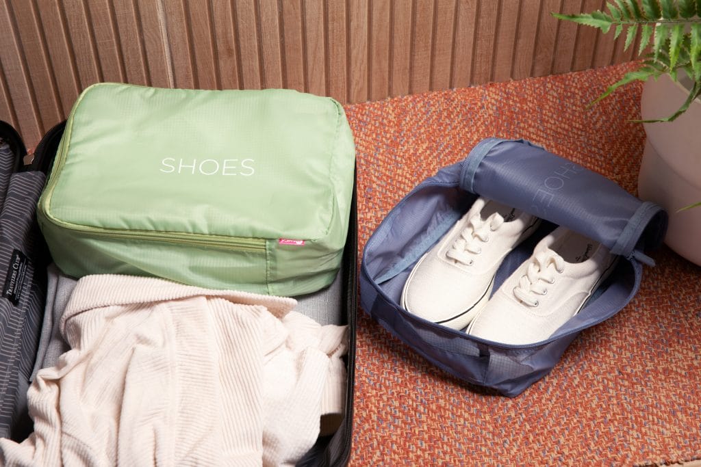 The Slate Green Packing Cube sits closed in a luggage case. The Slate Blue Packing Cube holds a pair of white shoes.